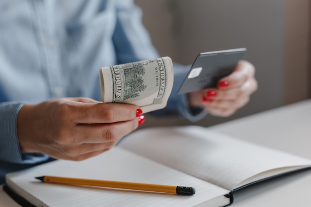 Primer plano de las manos de una mujer con uñas rojas sosteniendo billetes de cien dólares y una tarjeta de crédito negra