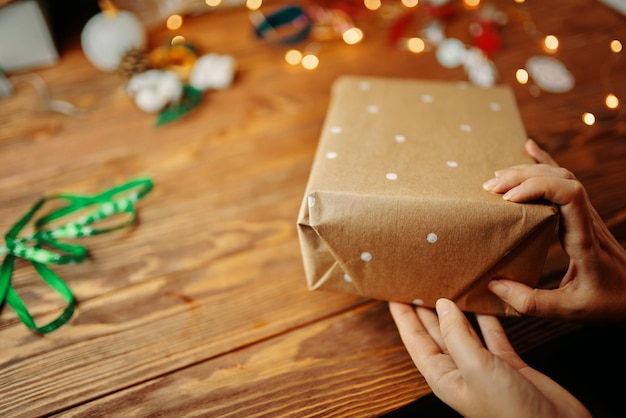 Primer plano de las manos de las mujeres embalaje regalo de navidad en la mesa de madera envolver papel artesanal con puntos blancos ...