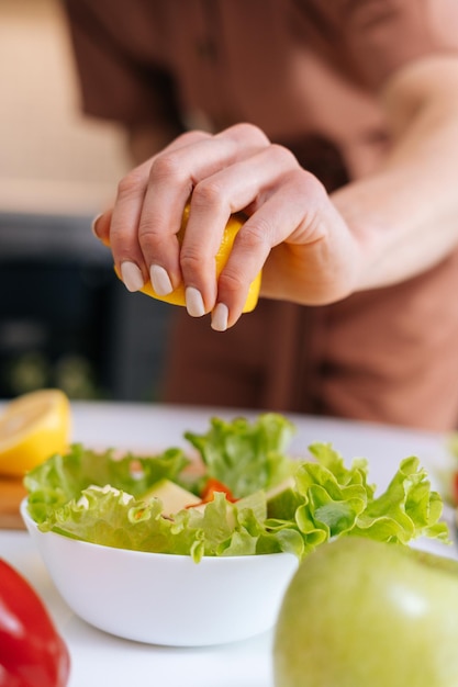 Primer plano de las manos de las mujeres exprimiendo jugo de limón amarillo fresco en una ensaladera con verduras en rodajas. Pimiento rojo, aguacate, limón sobre la mesa. Concepto de estilo de vida alimentario saludable.