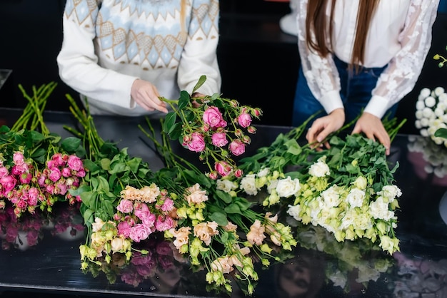 Primer plano de las manos de las mujeres recolectando y haciendo hermosos ramos festivos en una acogedora floristería Floristería y elaboración de ramos en una floristería Pequeña empresa