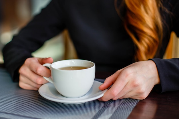 Primer plano de las manos de las mujeres con una taza de té verde mientras está sentado en un café cómodo