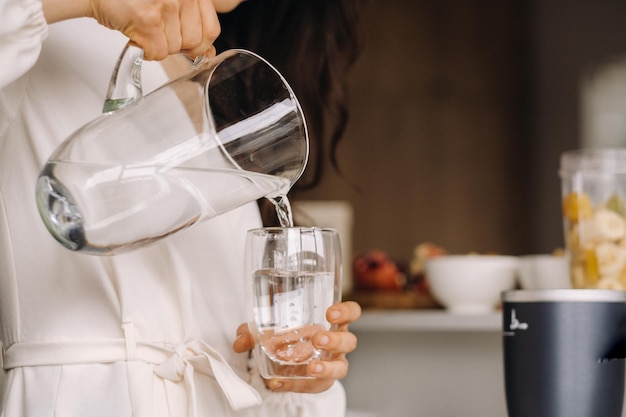 Primer plano de las manos de una niña en la cocina que vierte agua limpia en un vaso