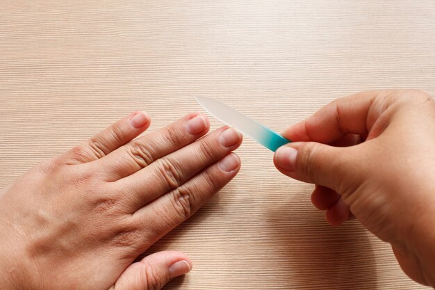 Primer plano de las manos, una niña haciendo una manicura a sí misma, lima de uñas azul.