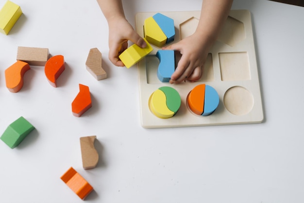 Primer plano de las manos de un niño irreconocible insertando bloques de madera en las ranuras del juguete educativo. Concepto de educación infantil.