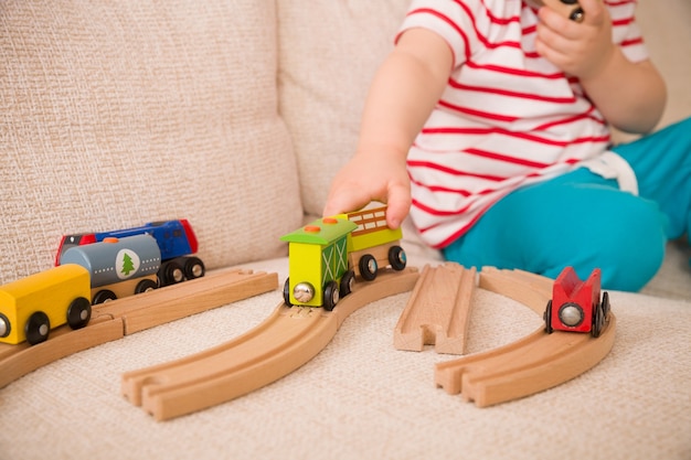 Primer plano de las manos del niño jugando con juguetes de madera tren y ferrocarril en el sofá