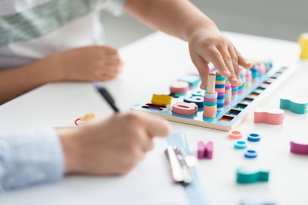 Primer plano de las manos de un niño pequeño jugando con un juego lógico de madera mujer profesional terapeuta tomando