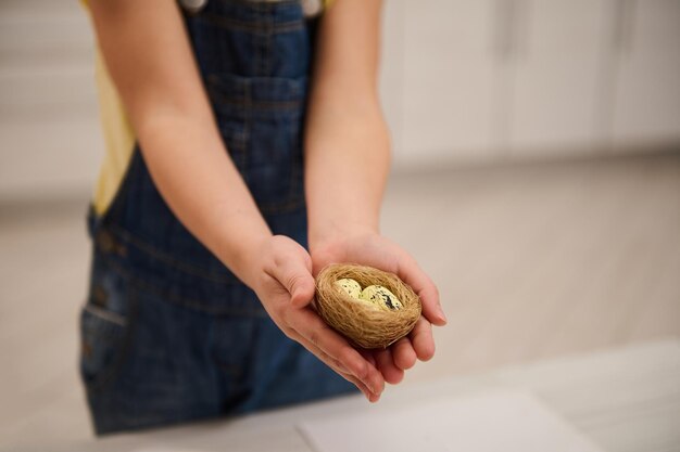 Primer plano de las manos del niño sosteniendo un nido de juguete con huevos Concepto de celebración de Pascua