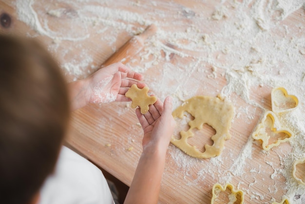 Primer plano de las manos de los niños que cortan una galleta en blanco de masa cruda en forma de oso