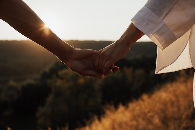 Primer plano de las manos de la pareja. Se toman de la mano al atardecer, sol.