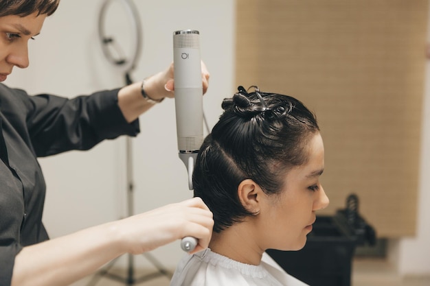 Primer plano de las manos de una peluquera secando el cabello de las mujeres con un secador de pelo corto y peinando