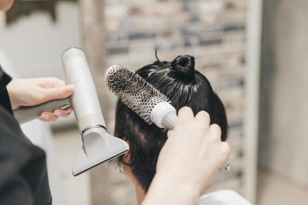Primer plano de las manos de una peluquera secando el cabello de las mujeres con un secador de pelo corto y peinando