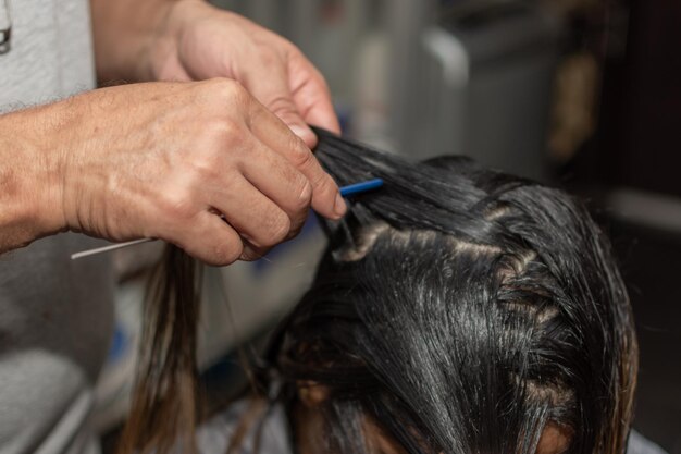 Primer plano de las manos de un peluquero profesional preparando el cabello de una mujer para teñir el enfoque selectivo