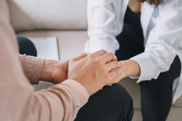 Primer plano de las manos del psiquiatra juntas sosteniendo la palma de su paciente. Hombre psicológico reconfortante y sosteniendo una mano de mujer mientras se sienta en el sofá. concepto de psicólogo