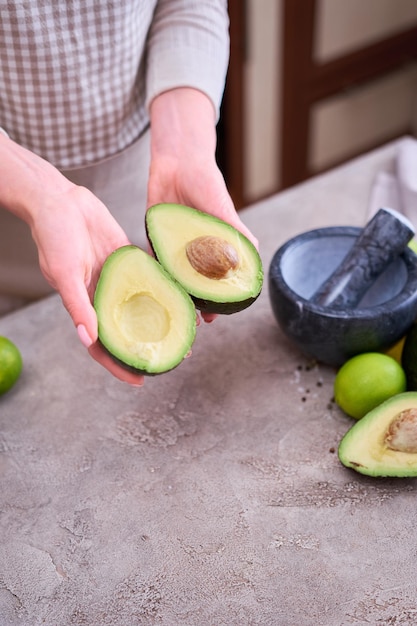 Primer plano de manos sosteniendo aguacate fresco cortado por la mitad sobre una mesa de hormigón gris