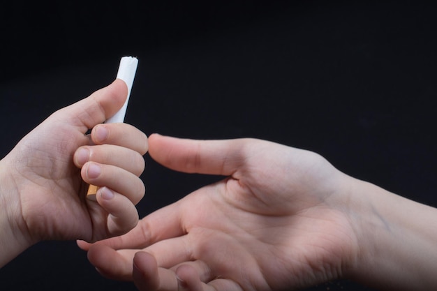 Foto primer plano de manos sosteniendo cigarrillos contra un fondo negro