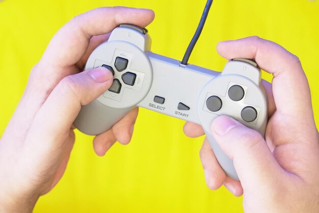 Primer plano de manos sosteniendo el controlador de juego contra un fondo amarillo