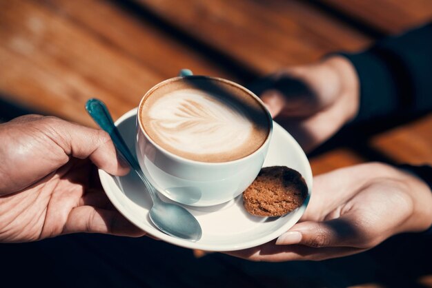 Primer plano de manos sosteniendo y dando un capuchino o blanco plano a un cliente en un café Bebida caliente con imagen de planta creativa en espuma de leche Una bebida de café por la mañana hecha por un barista en un restaurante