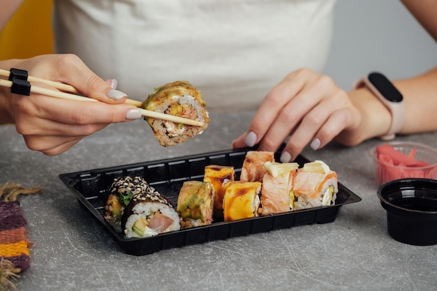 Primer plano de manos sosteniendo rollo de sushi con palillos