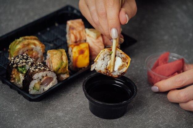 Foto primer plano de manos sosteniendo rollo de sushi con palillos