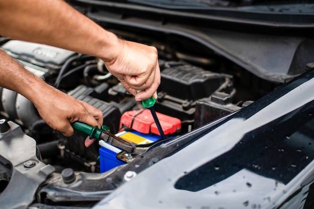 En primer plano las manos de un técnico masculino están usando una herramienta para reemplazar la batería del coche estacionado en casa coche negro la batería está dañada las herramientas tienen pinzas y destornilladores