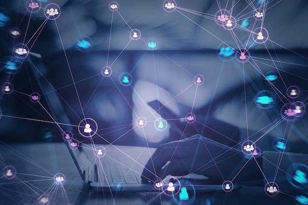 Primer plano de las manos usando una computadora portátil y un teléfono con íconos de equipo de personas digitales conectados sobre un fondo púrpura borroso Red digital comunidad en línea y concepto de redes sociales Doble exposición