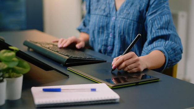 Primer plano de las manos usando tableta gráfica con lápiz y teclado en la computadora para retocar imágenes en el estudio. Artista de fotografía que trabaja con tecnología y equipos de edición.