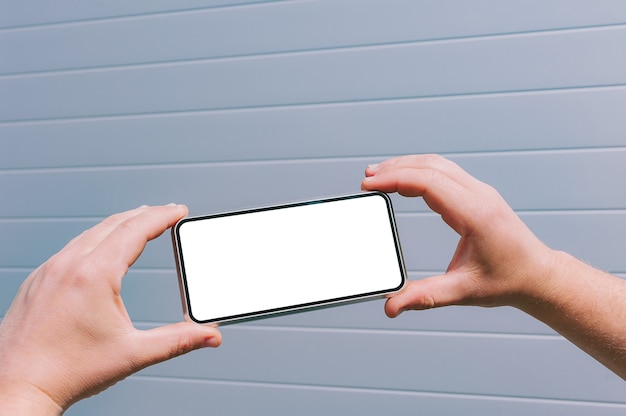 Primer plano, maqueta de un teléfono inteligente en manos de un hombre. contra el fondo de una pared gris.