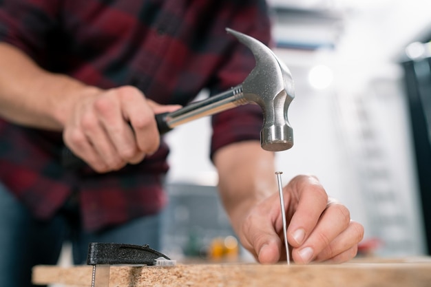 Primer plano de martillar un clavo en la tabla Un carpintero con una camisa de franela roja, jeans y guantes protectores de tela clava las tablas de madera