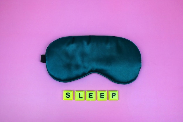 Foto primer plano de la máscara para dormir de satén verde suave y limpio aislado en rosa con la palabra concepto de autocuidado del sueño