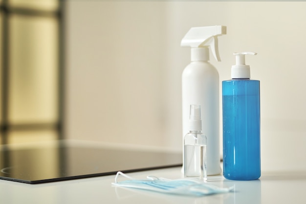 Primer plano de mascarilla protectora y botellas de desinfectante para limpiar superficies en la cocina