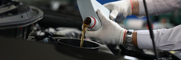 Primer plano de un mecánico experimentado que verifica y vierte aceite en un orificio especial en el automóvil