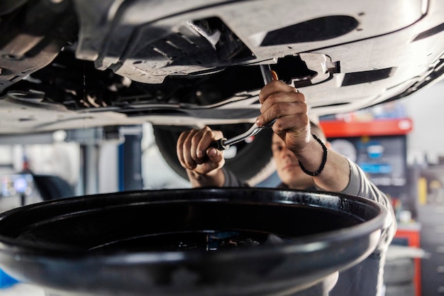 Foto primer plano de un mecánico que desenrosca el perno en la parte inferior del automóvil con una llave descentrada