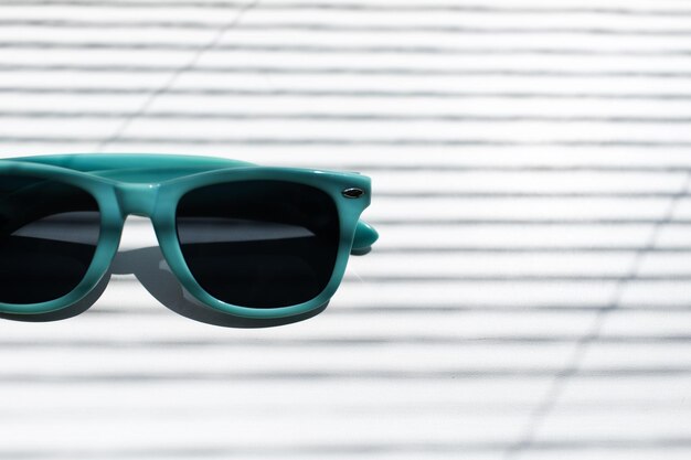 Primer plano de medias gafas de sol de color azul sobre fondo blanco rayado por sombras