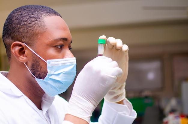 Primer plano de un médico africano en el laboratorio mirando de cerca la vacuna en su mano