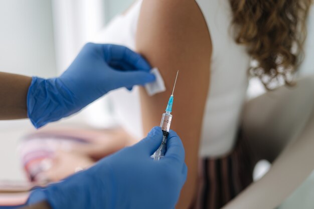 Primer plano de un médico en guantes protectores sosteniendo una jeringa y usando algodón antes de hacer la inyección para