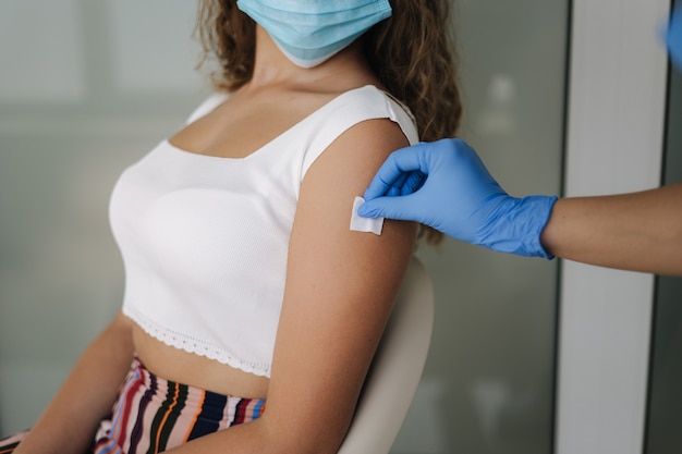 Primer plano de un médico en guantes protectores sosteniendo una jeringa y usando algodón antes de hacer la inyección para