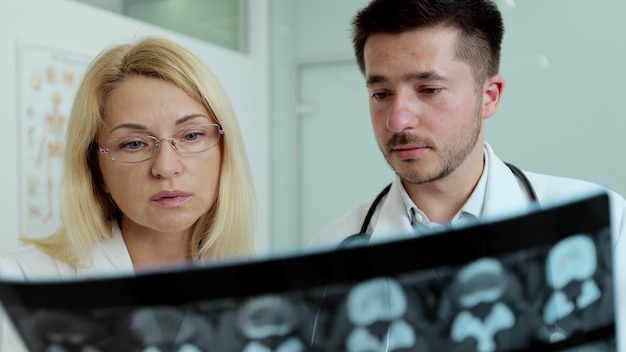 Primer plano médico masculino y colega examinando los pulmones de la película de rayos x de tórax del paciente en el departamento de radiología del hospital. Prueba de rayos x covid-19, concepto de cámara lenta de epidemia de virus covid en todo el mundo.