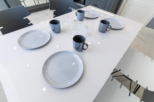 Primer plano de una mesa blanca con tazas y platos grises en la cocina