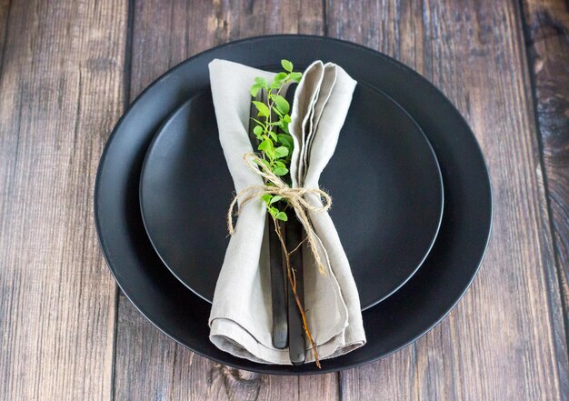 Primer plano de la mesa con plato negro cubiertos negros y servilleta de lino en la mesa de madera