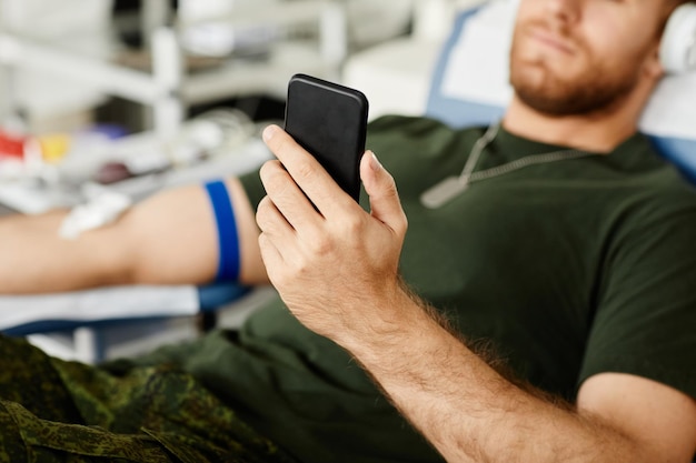 Primer plano de un militar que da sangre mientras se sienta en una silla en el centro de donación de sangre y sostiene sma
