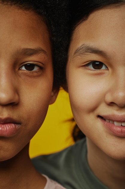 Primer plano de la mitad de las caras de dos niñas multiculturales jóvenes con cabello oscuro y ojos marrones mirando c