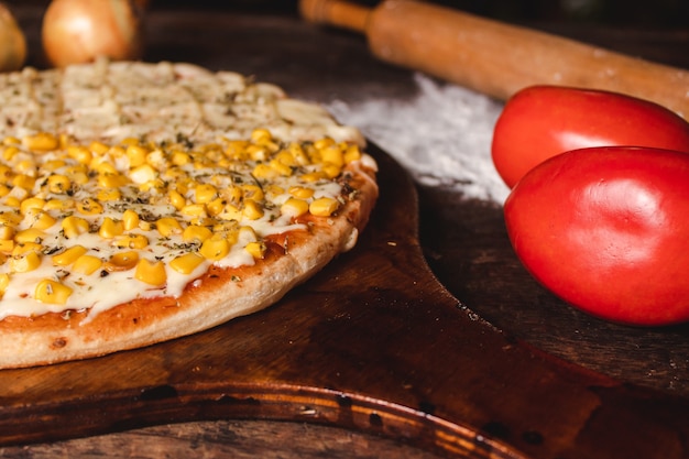 Foto primer plano de una mitad de maíz mitad pizza de queso mozzarella con tomate en una mesa de madera.