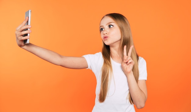 Primer plano de moda elegante hermosa chica rubia en camiseta blanca mientras hace foto selfie en su teléfono inteligente aislado en estudio