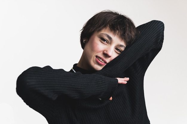 Primer plano de una modelo femenina con el pelo corto en un jersey negro inclinando la cabeza sobre un brazo y