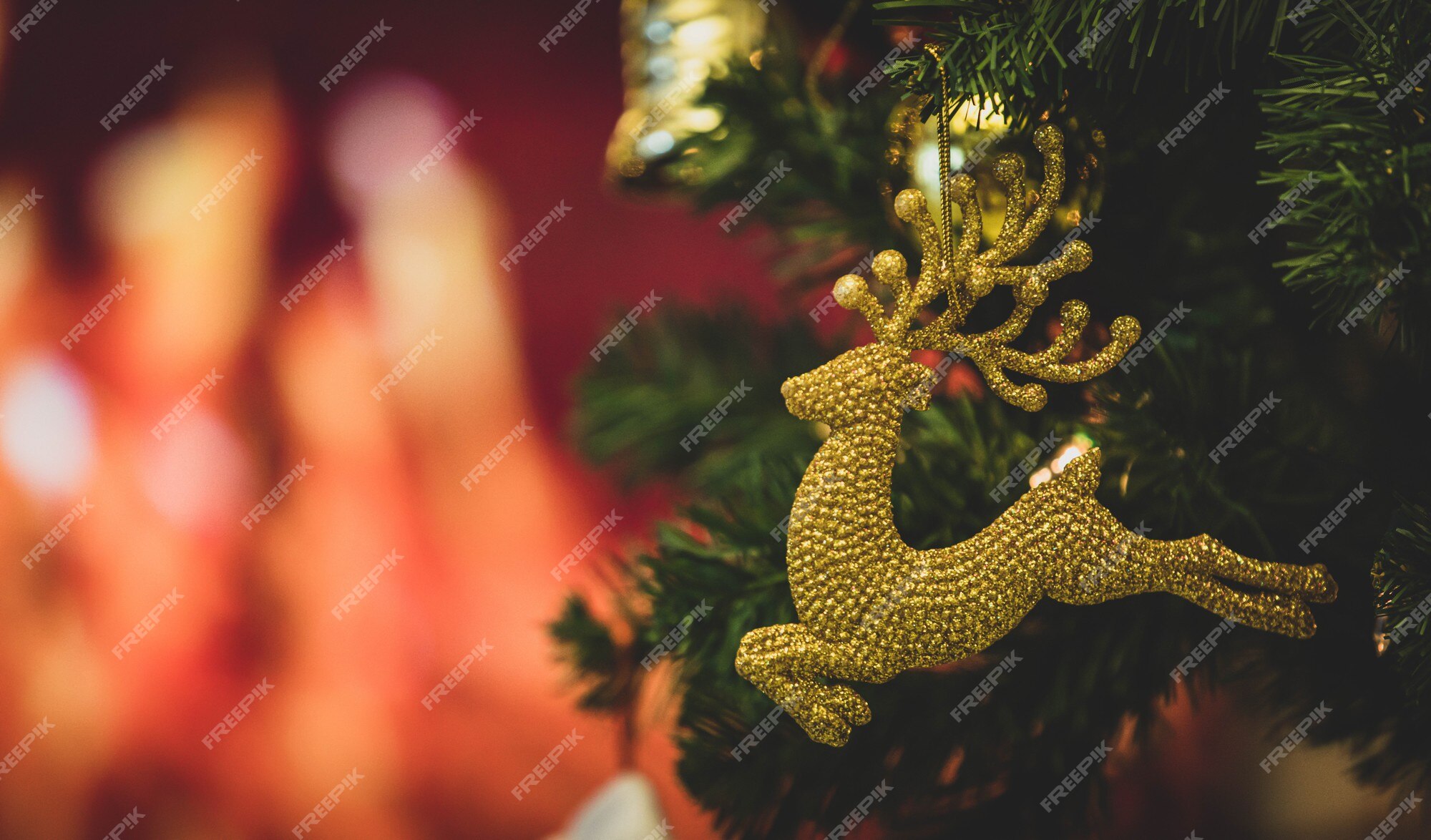 Primer plano del modelo de reno de decoración de nochebuena rojo brillante  que cuelga decorando en la rama de árbol de pino de navidad verde con bolas  de esfera y otras cosas