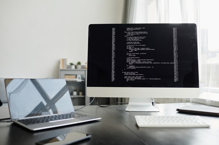 Foto primer plano del monitor de la computadora con carga de software y computadora portátil en el lugar de trabajo en la oficina