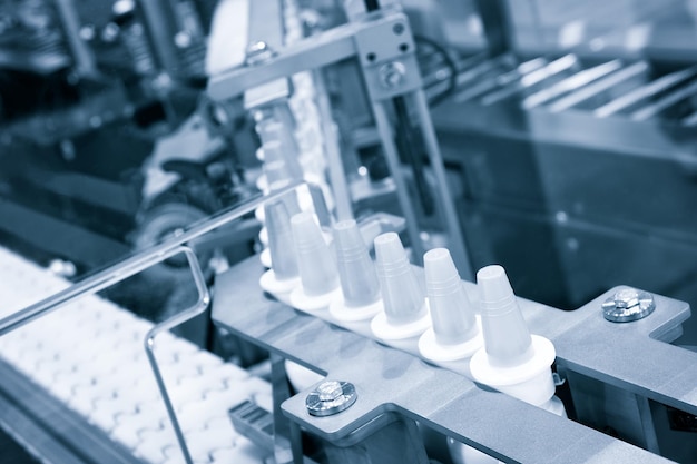 Primer plano Muchas botellas de spray de plástico blanco para envasar medicamentos líquidos o cosméticos en una fila en una cinta transportadora en una fábrica de fabricación de productos farmacéuticos