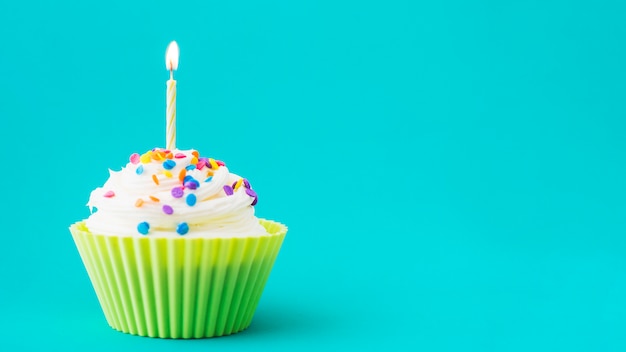 Foto primer plano de muffin con vela iluminada sobre fondo turquesa