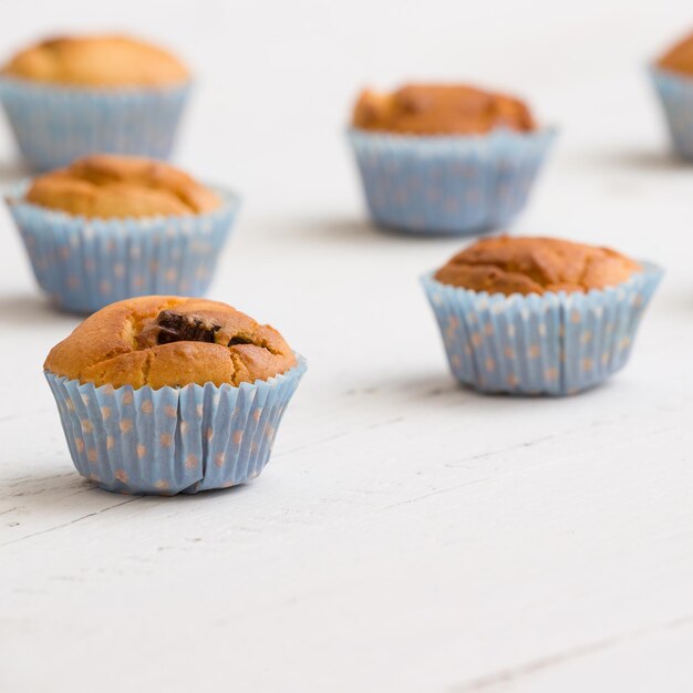 Primer plano de muffins de vainilla caseros en vasos de papel azul sobre fondo blanco de madera