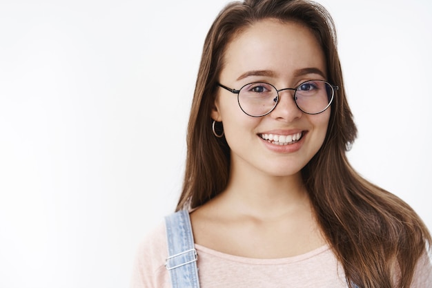 Primer plano de una mujer de 20 años atractiva y linda amigable con gafas con cabello castaño sonriendo alegremente con expresión esperanzada y emocionada divirtiéndose, riendo y pasando tiempo en compañía divertida.